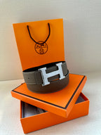 Leather belt with textured gray strap and silver-tone H buckle on a stand.
