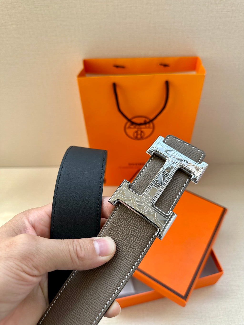 Leather belt with textured gray strap and silver-tone buckle detail, held in hand.