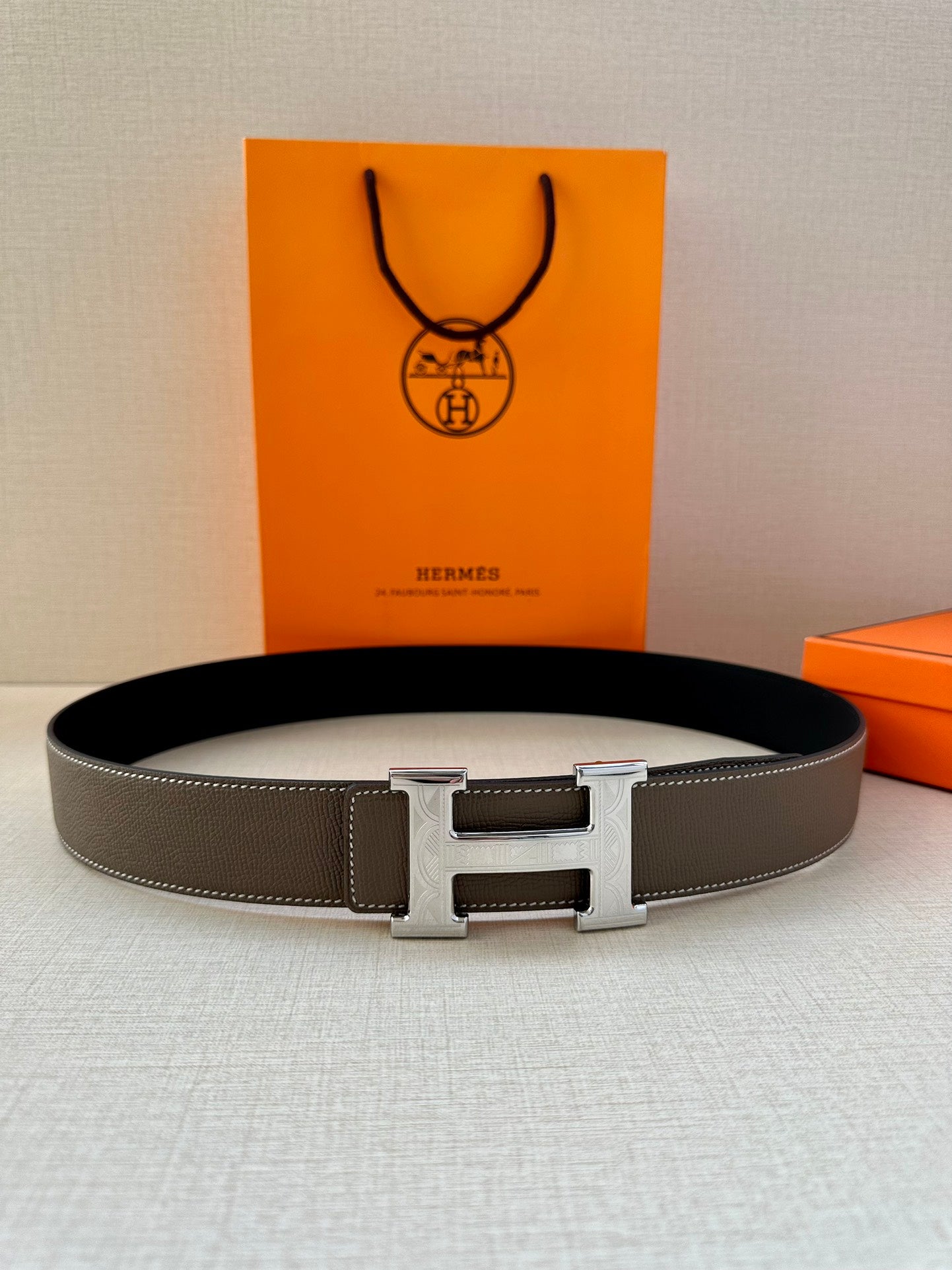 Leather belt with textured gray strap and silver-tone H buckle, laid flat.