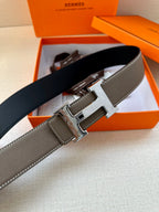 Leather belt with textured gray strap and silver-tone buckle, close-up of buckle face.