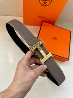 Leather belt with textured gray strap and gold-tone H buckle.