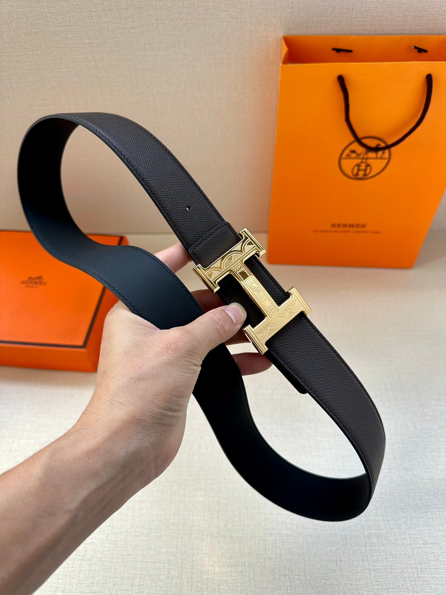 Black leather belt with gold-tone H buckle, strap shown coiled in hand.