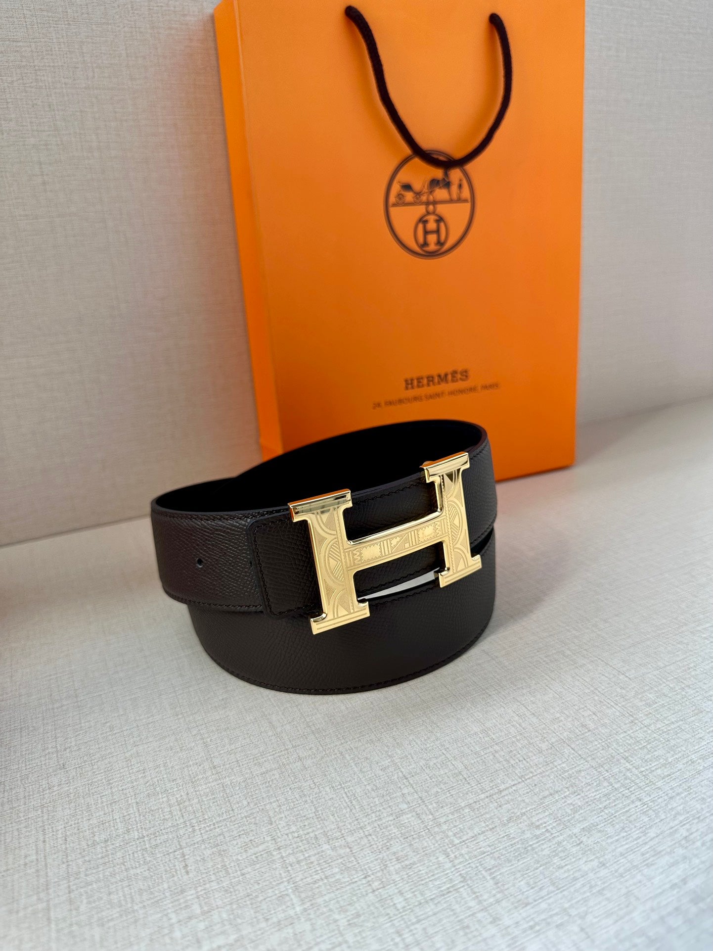 Black leather belt with gold-tone H buckle, laid flat with buckle centered.