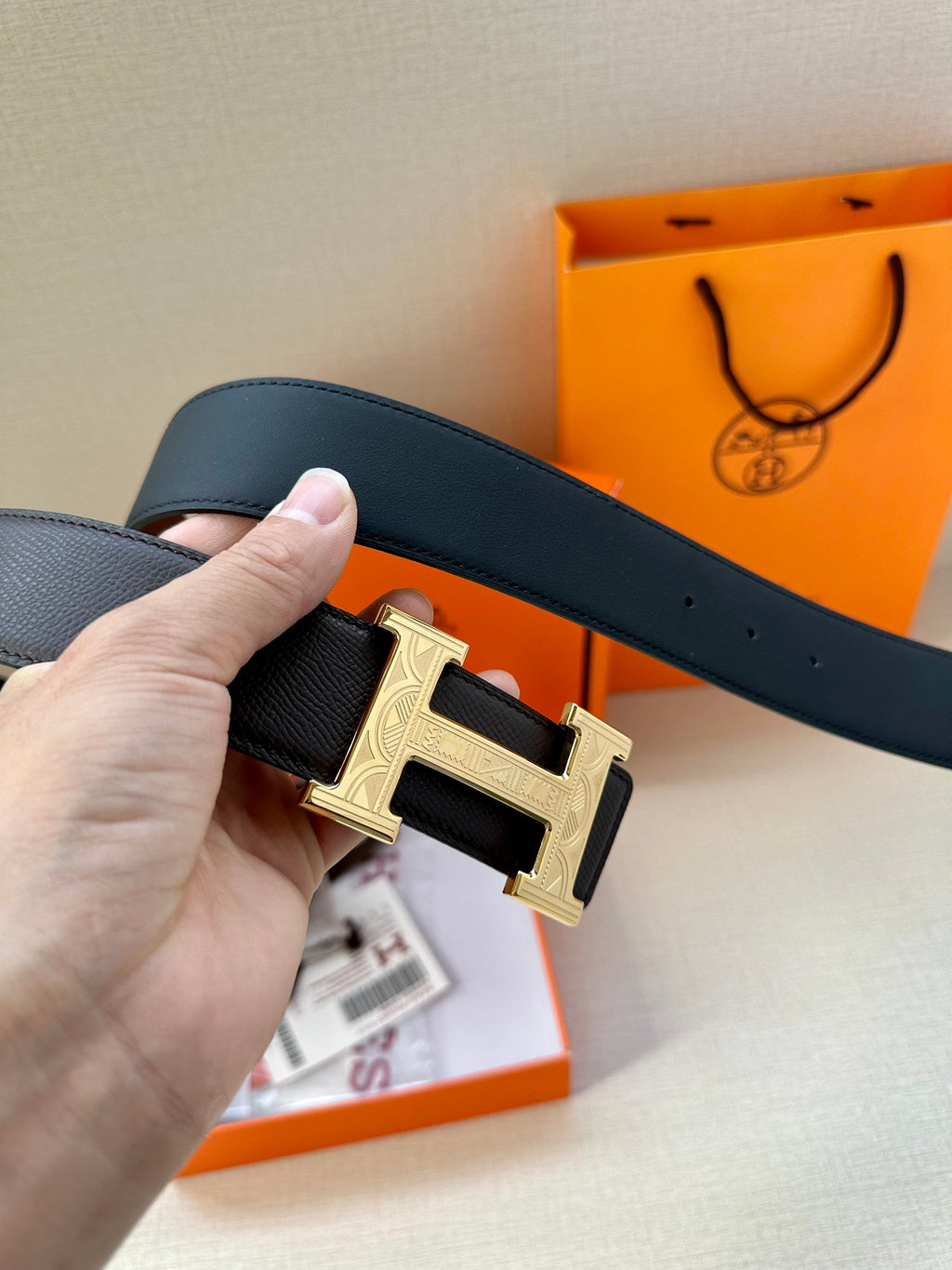 Black leather belt with gold-tone H buckle, close-up of buckle and strap.