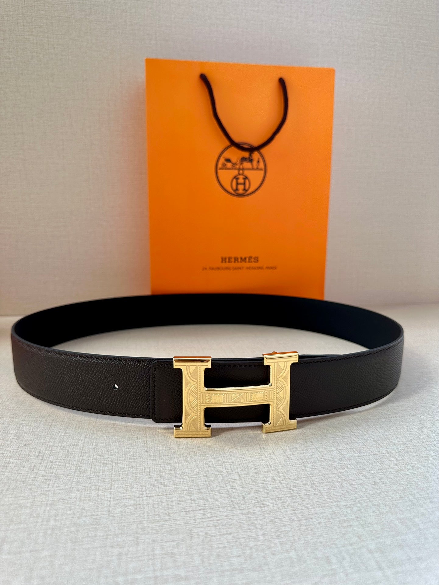 Black leather belt with gold-tone H buckle, laid flat, buckle facing up.