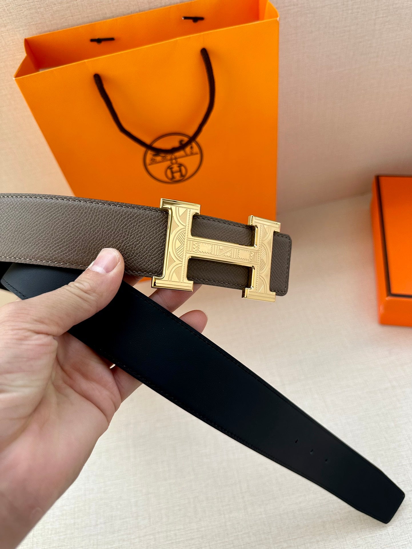 Gray leather belt with gold-tone H buckle and black lining on strap