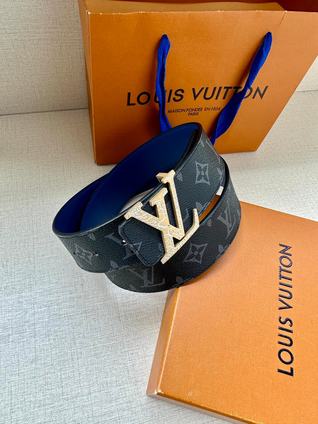 Louis Vuitton wide monogram belt with dark blue strap and gold LV buckle.