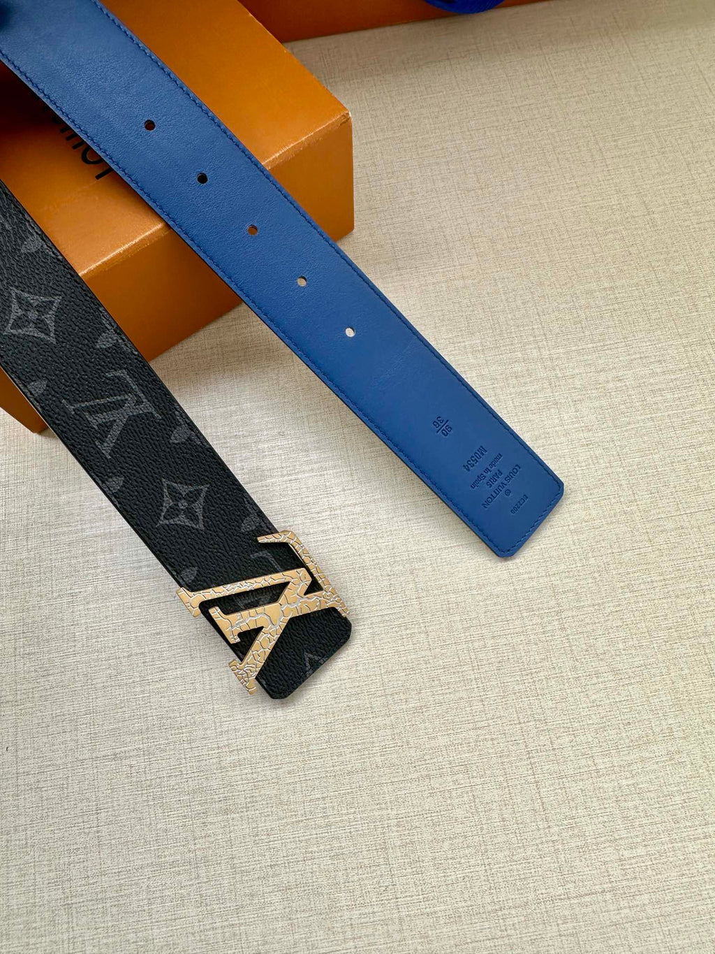 Louis Vuitton belt pair: dark blue monogram belt and light blue smooth belt, laid out.
