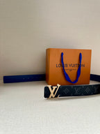 Louis Vuitton monogram belt with gold LV buckle and dark blue strap beside orange box.