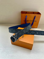 Louis Vuitton monogram belt with dark blue strap and gold-tone LV buckle, near gift boxes.