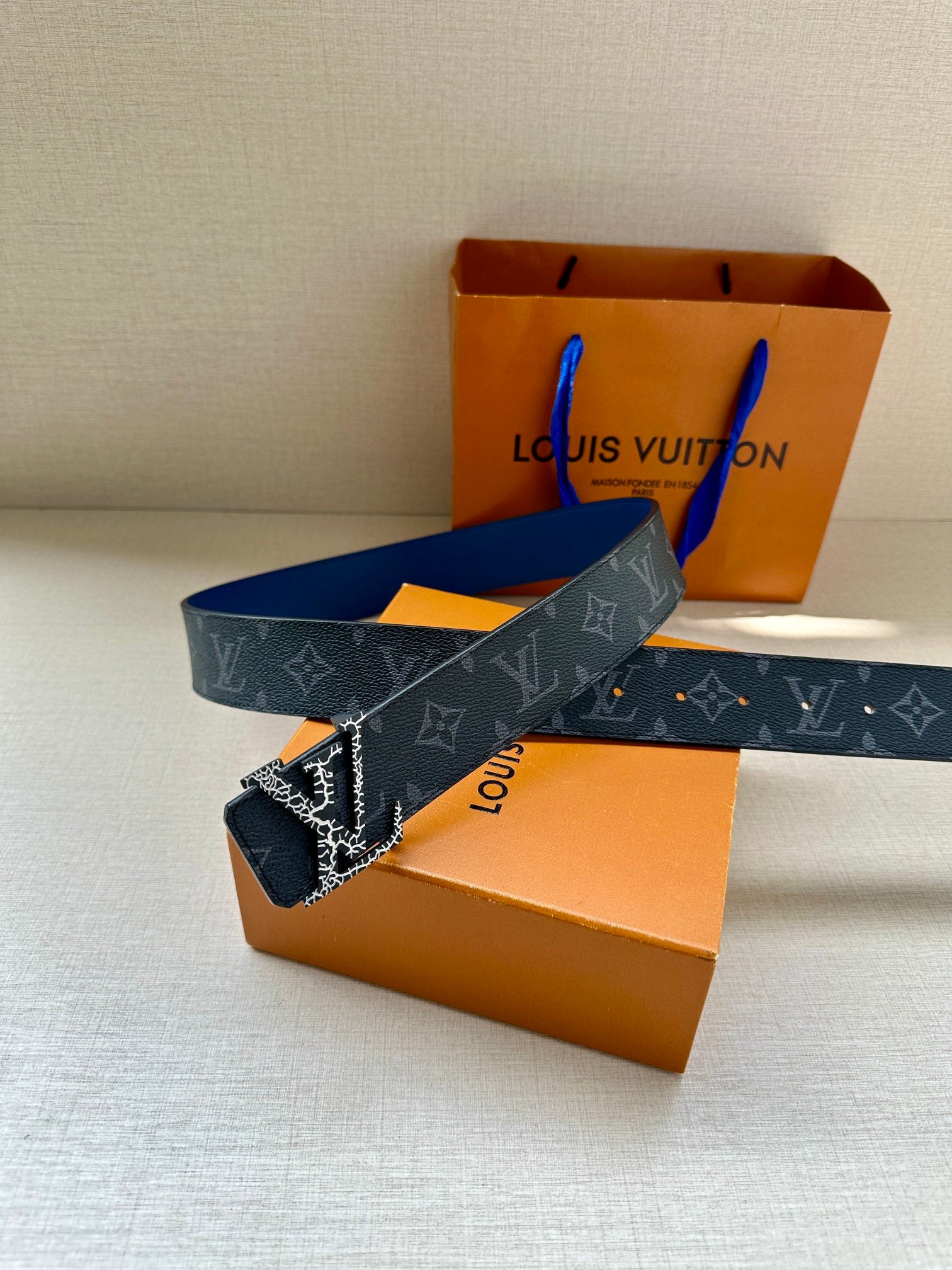 Louis Vuitton monogram belt with dark blue strap and gold-tone LV buckle, near gift boxes.
