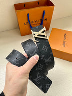 Louis Vuitton monogram belt held by hand, dark blue strap with gold LV buckle.