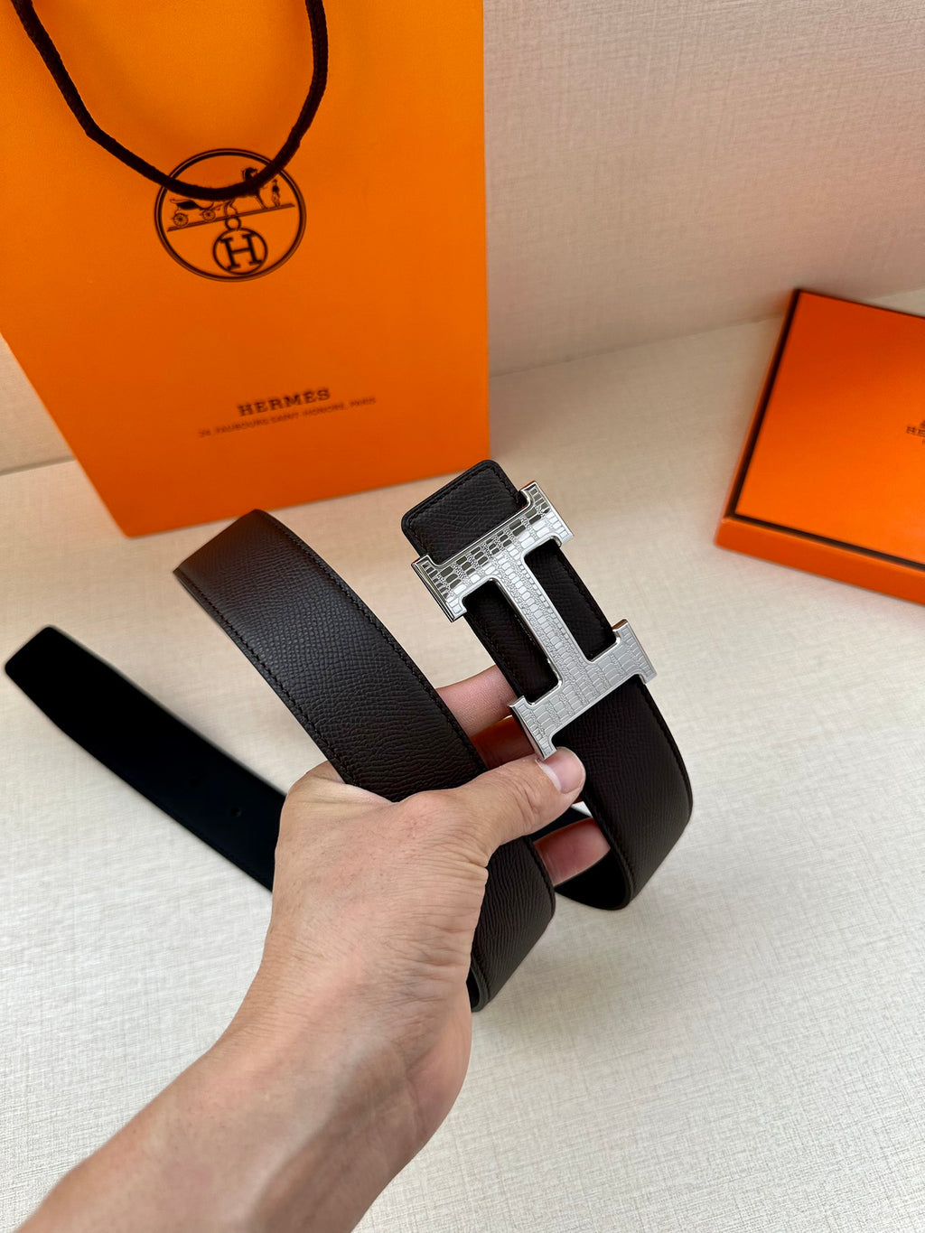 Hermes belt with dark leather strap and wide silver H buckle, front view held.