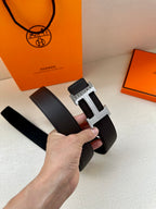 Hermes belt with dark leather strap and wide silver H buckle, front view held.