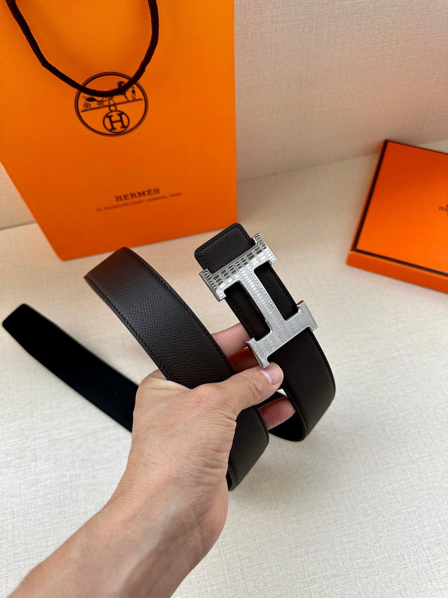 Hermes belt with dark leather strap and wide silver H buckle, front view held.