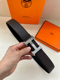 Hermes leather belt with dark strap and silver-toned H buckle, shown close-up.