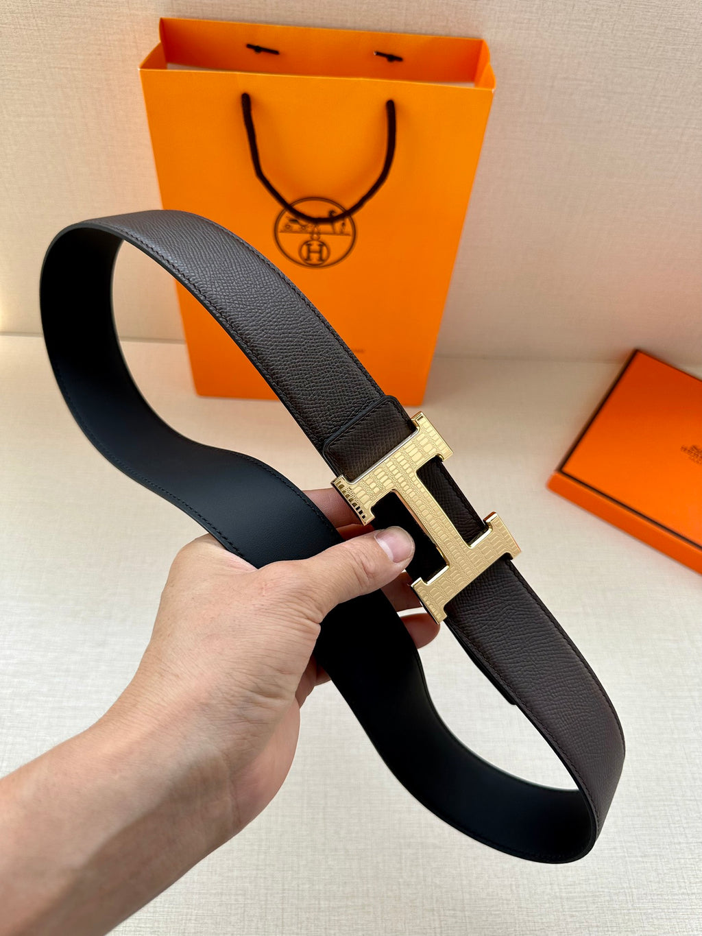 Hermes belt on hand: dark leather strap with silver-toned H buckle, side angle.