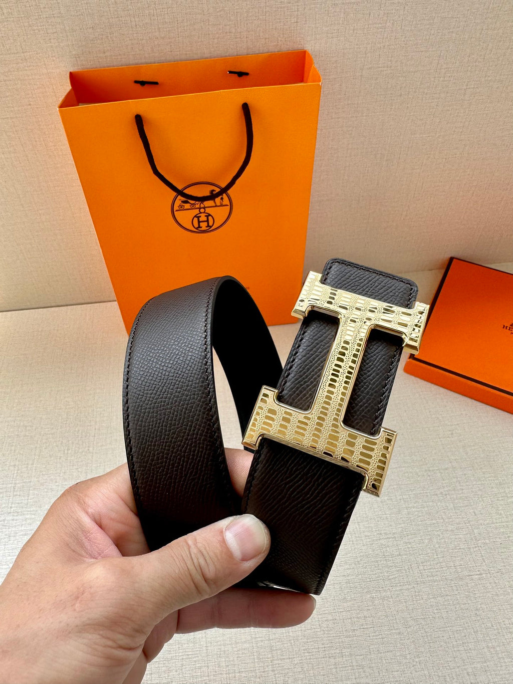 Hermes belt detail with dark strap and gold-tone H buckle with engraved pattern.