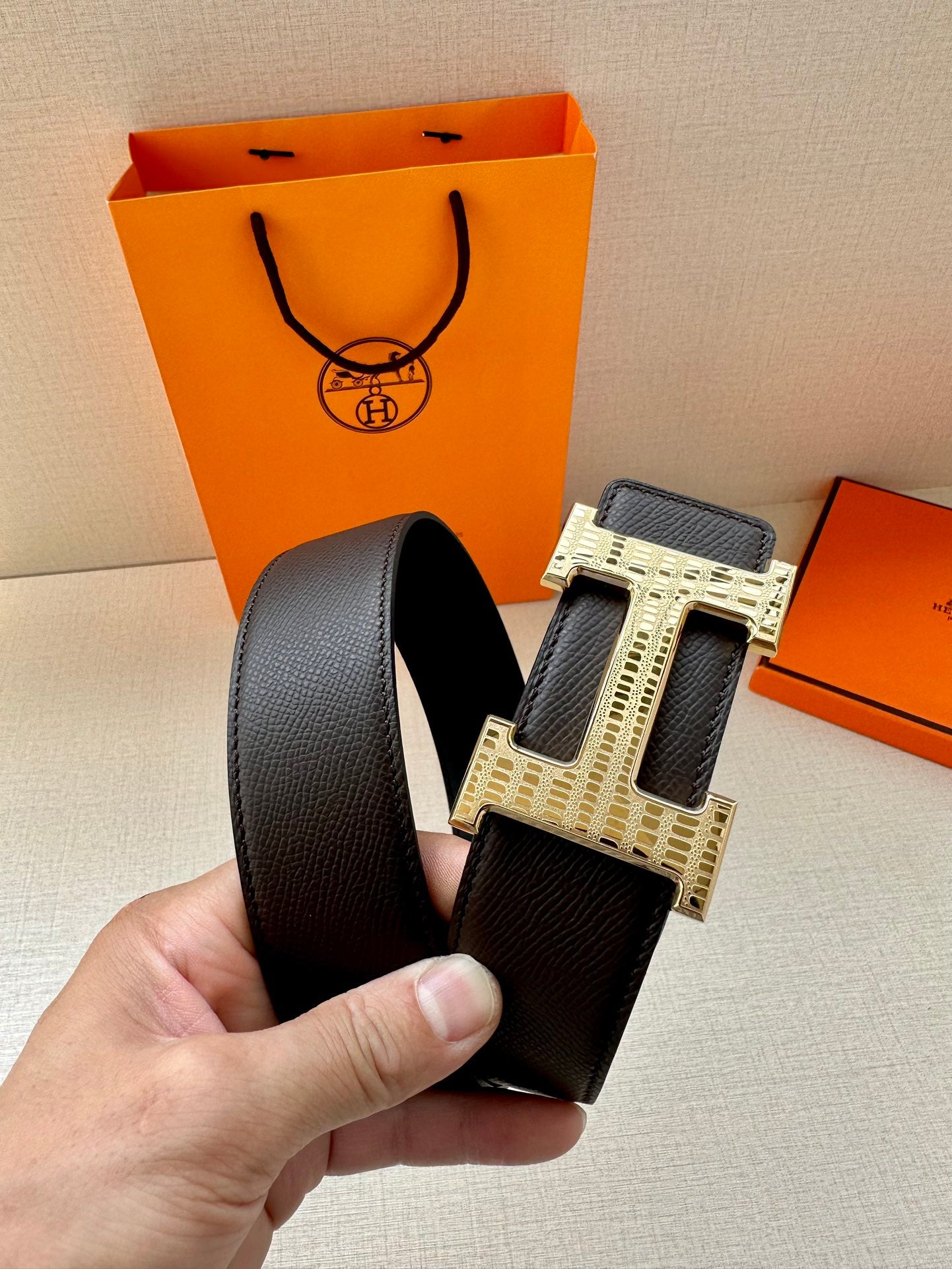 Hermes belt detail with dark strap and gold-tone H buckle with engraved pattern.
