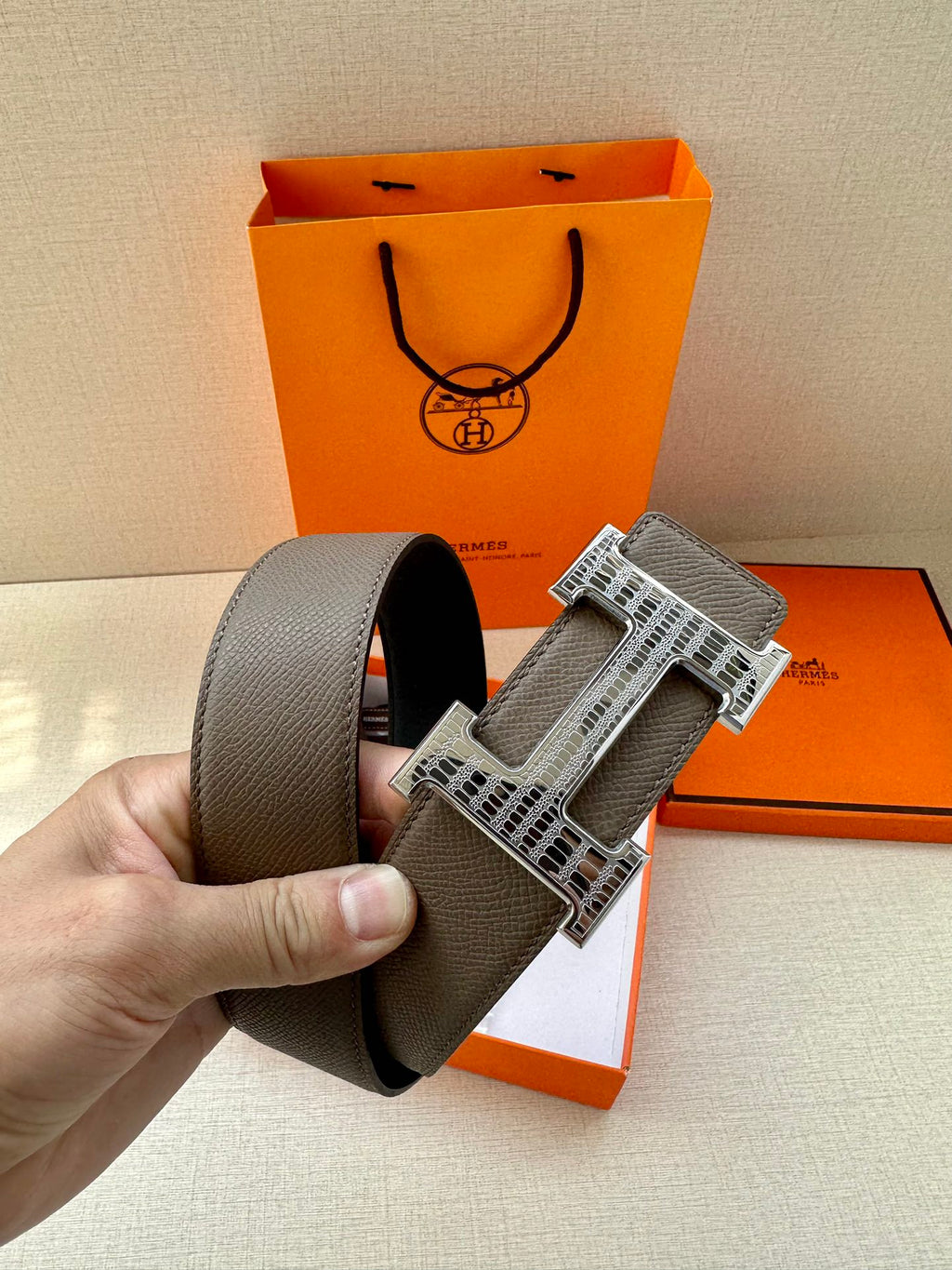 Gray leather belt with silver-tone H buckle, held for display