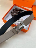 Gray leather belt with silver-tone H buckle, laid across packaging