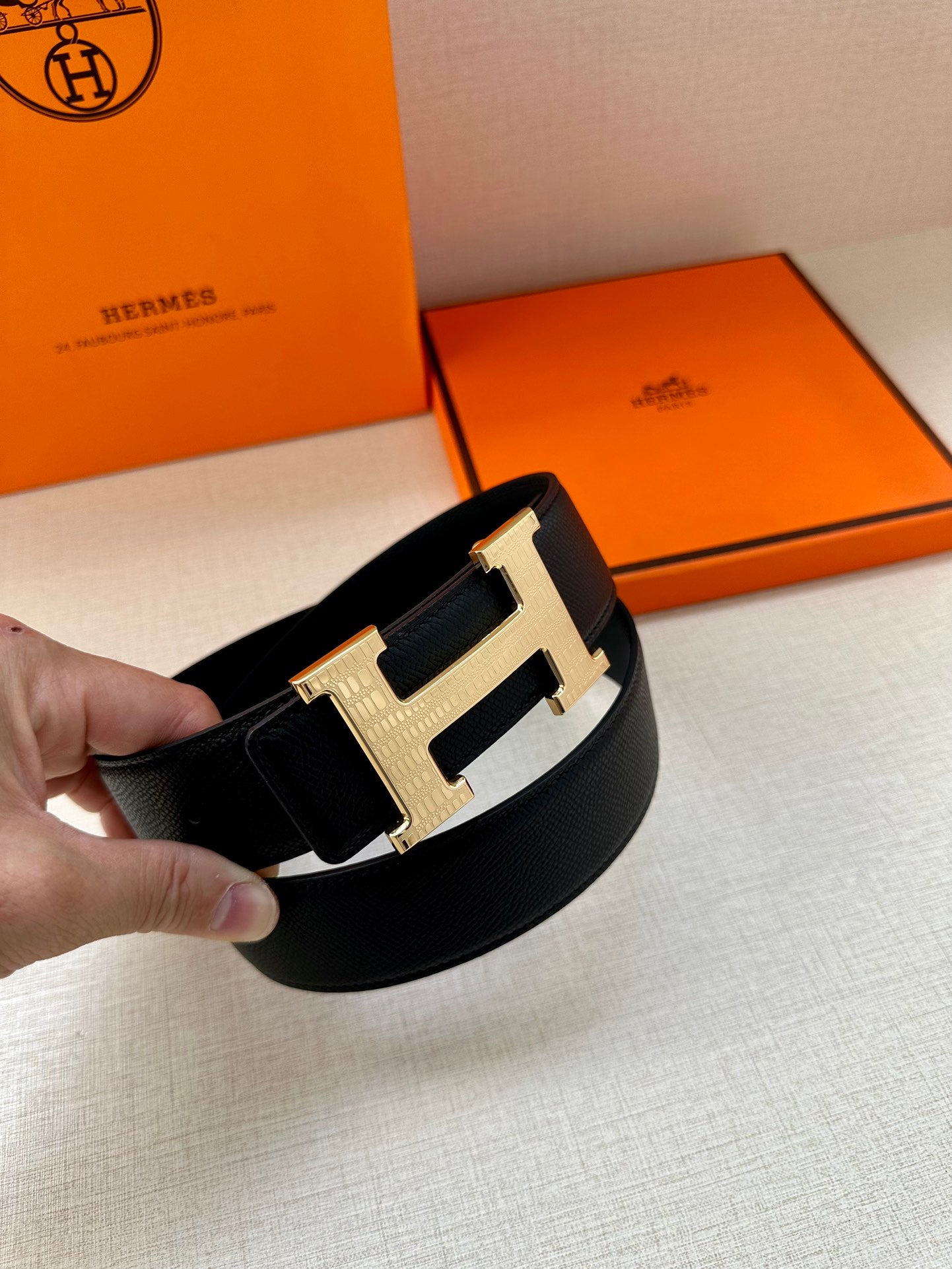 Black leather belt with large silver-tone buckle, held close-up