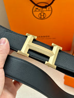 Hermes leather belt close-up: dark strap with gold-toned H-style buckle centerpiece.