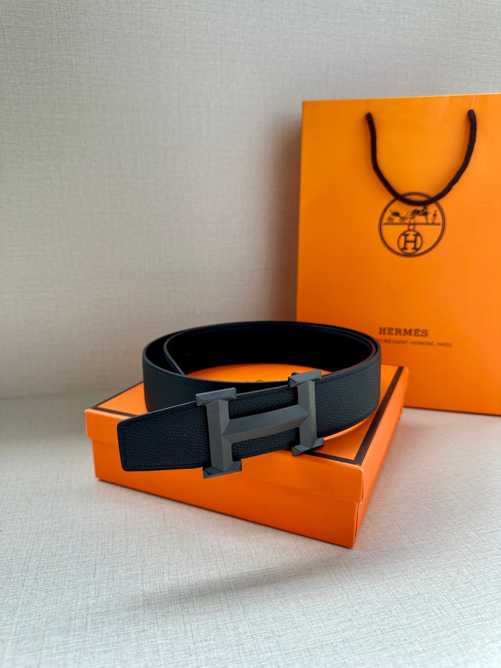 Hermes dark leather belt with flat silver-tone buckle on top of an orange box.
