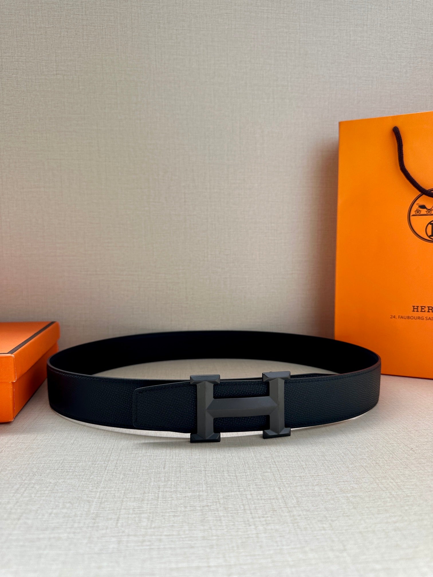 Hermes dark leather belt with silver-tone buckle on a box, viewed from above.