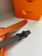 Leather belt buckle close-up: textured strap with silver-tone H hardware.