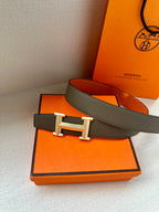 Leather belt with textured dark strap and silver-tone H buckle, resting on box.