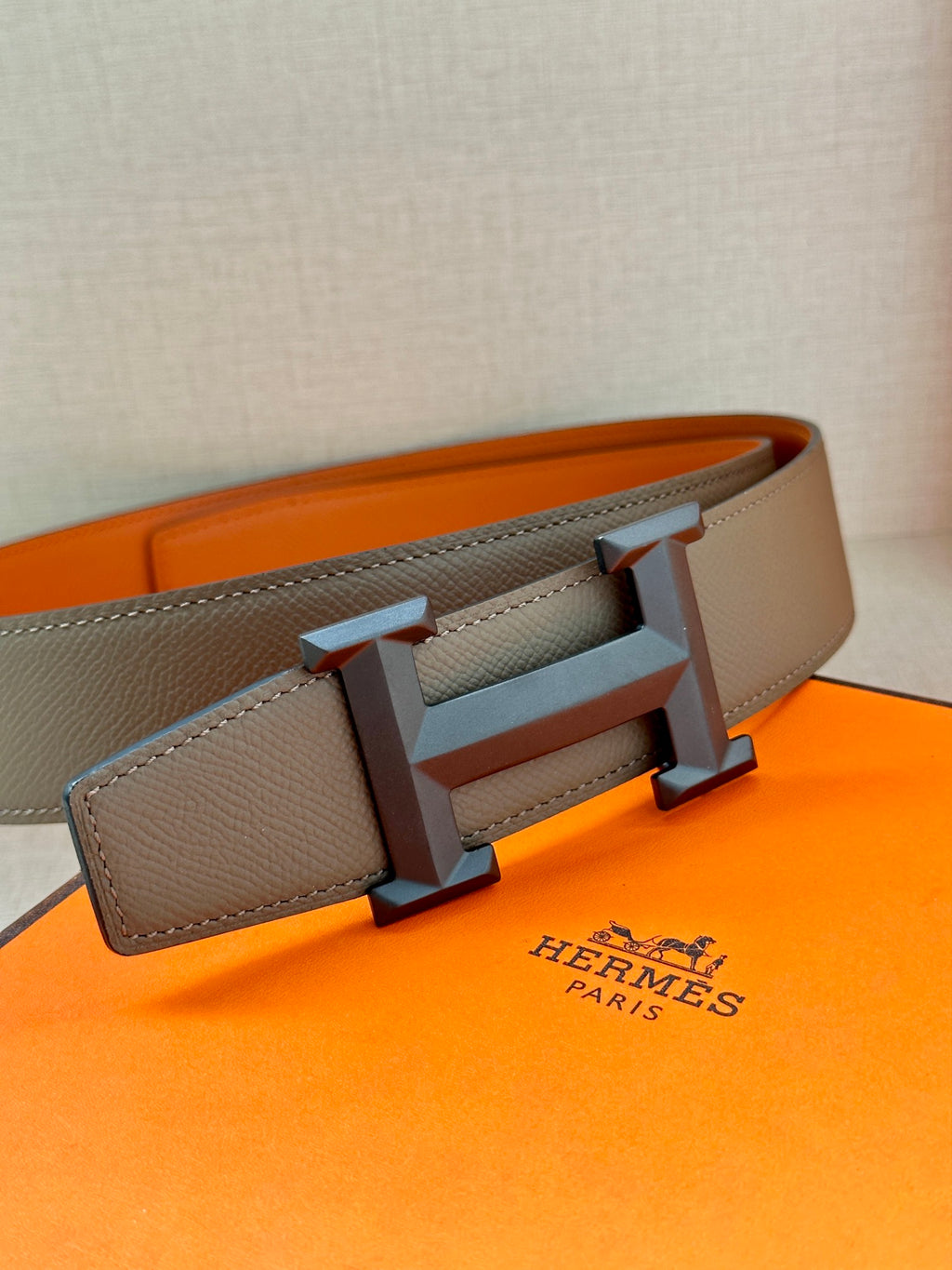 Leather belt close-up: textured strap with silver-tone H buckle, dark gray.
