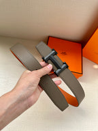 Leather belt held in hand with textured dark gray strap and silver-tone H buckle.