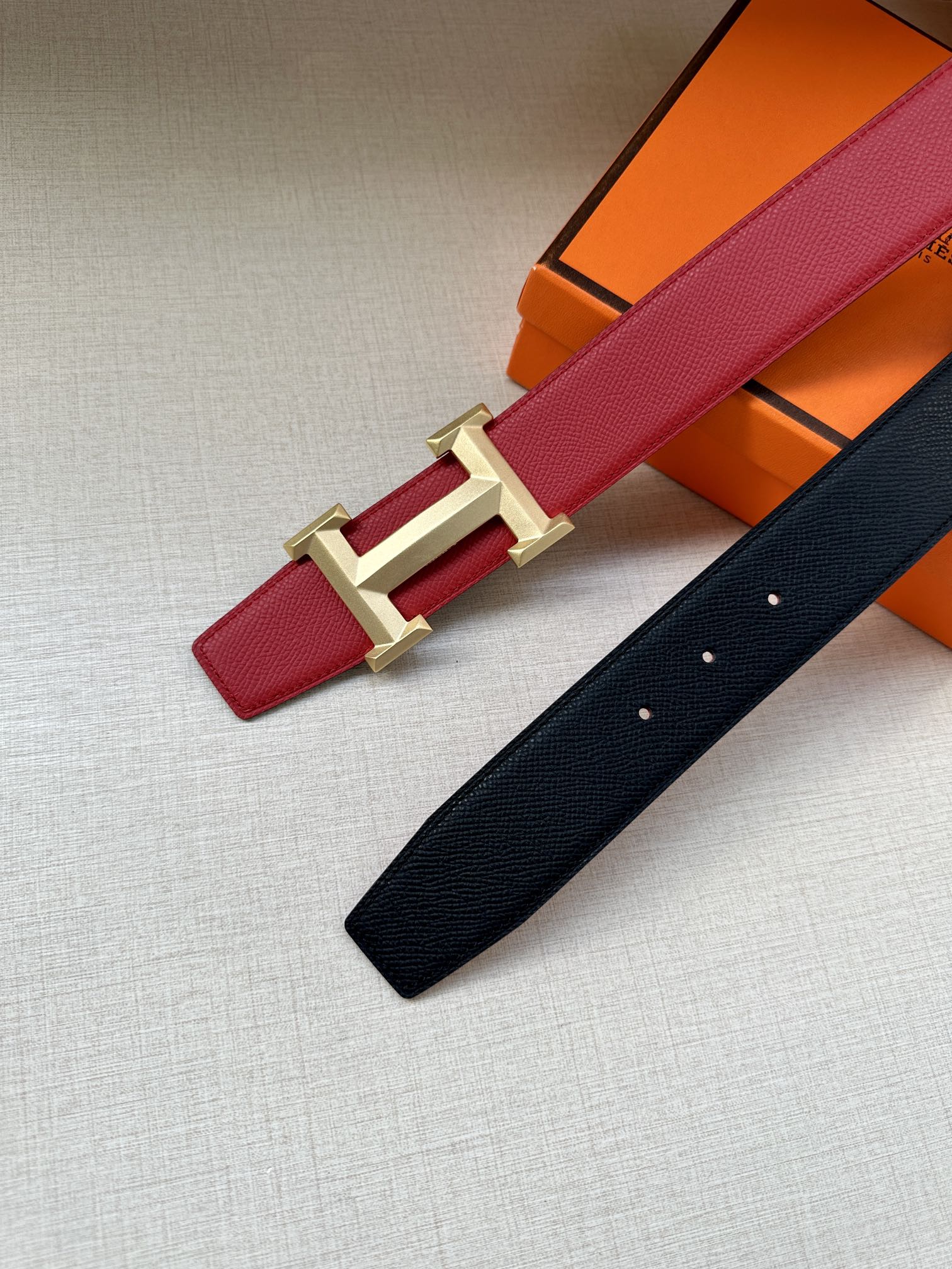 Red leather belt with gold H buckle, shown beside a dark leather belt.