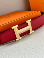 Red leather belt with gold H buckle, close side view with box nearby.