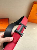 Red leather belt with dark H buckle and black strap section, close-up held in hand.