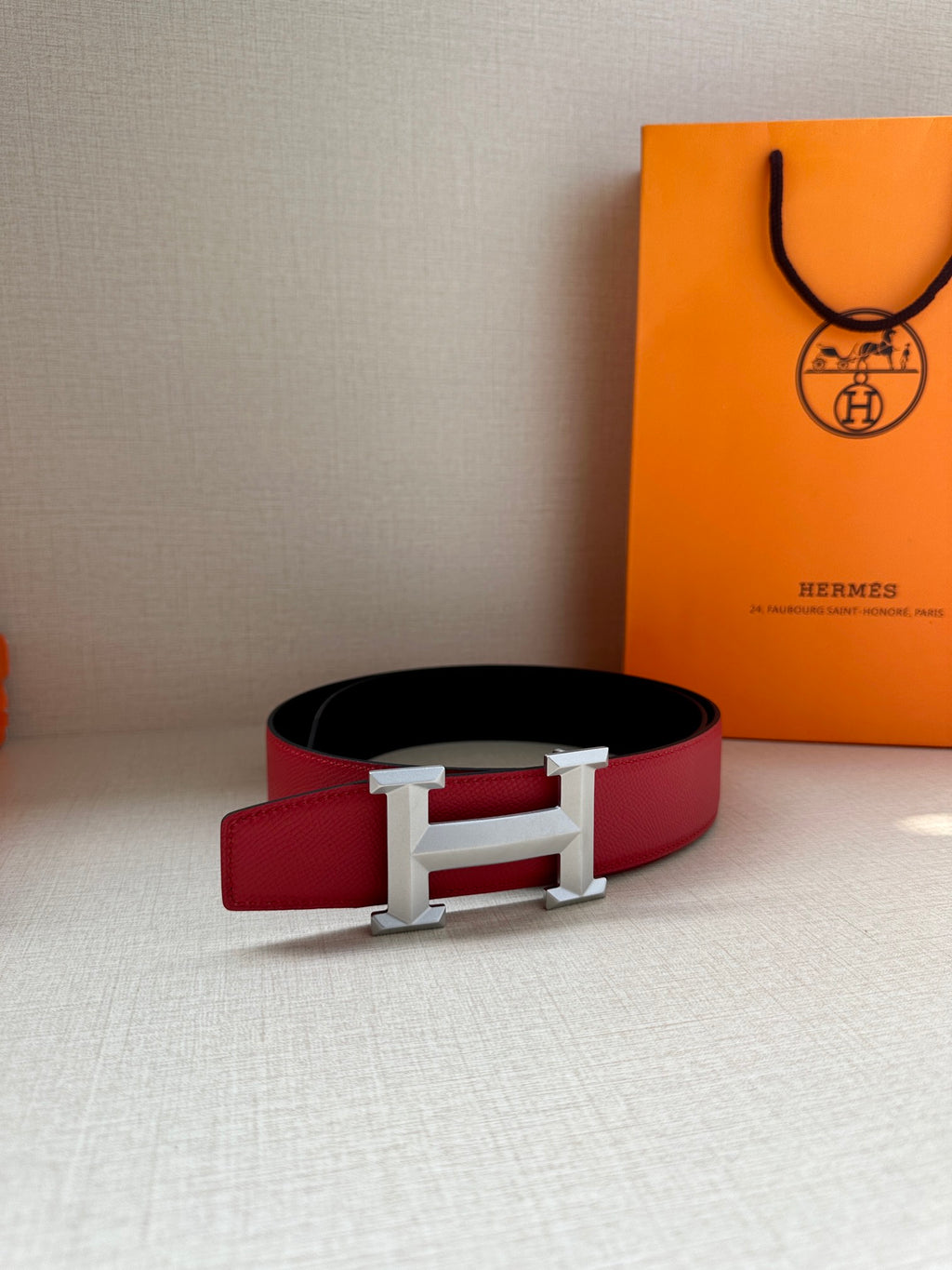 Red leather belt with silver-tone H buckle, resting flat with box nearby.