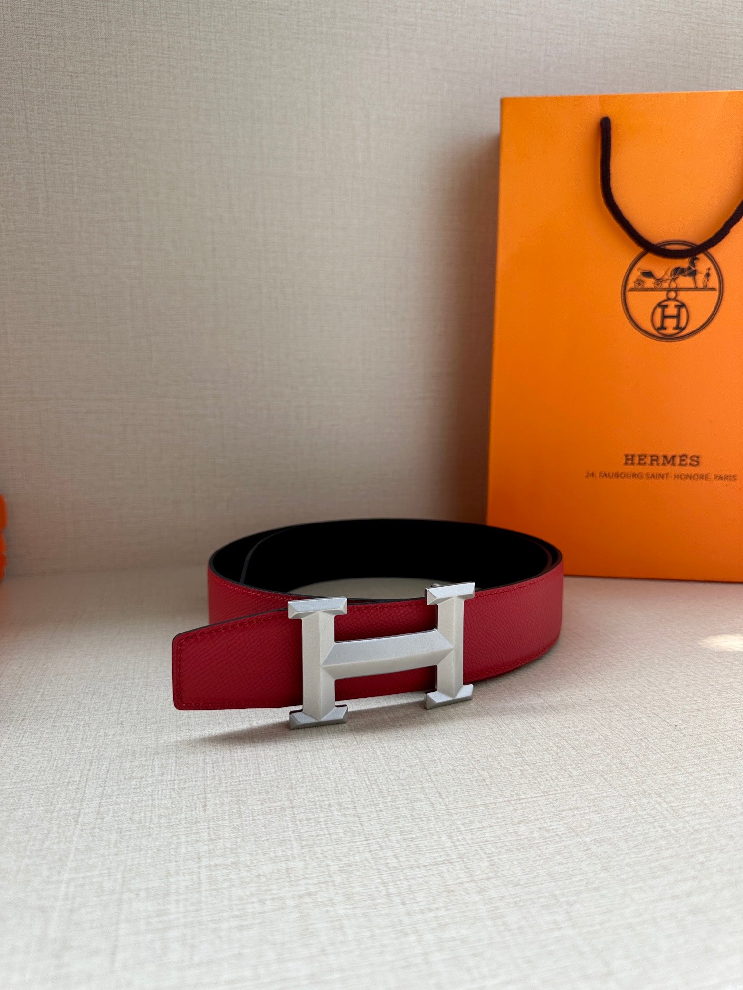 Red leather belt with silver-tone H buckle, resting flat with box nearby.