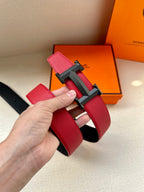 Red leather belt with dark H buckle, hand holding the strap end.