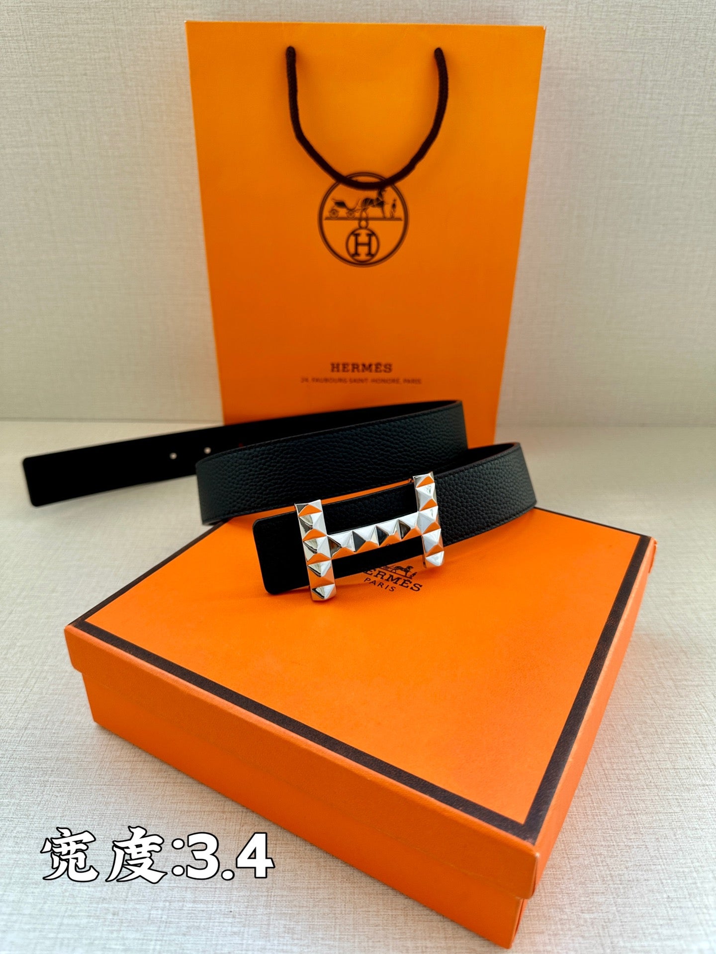 Black leather belt with silver-tone H buckle on top of an orange box.