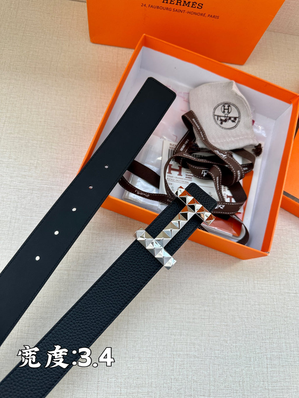 Black leather belt with silver-tone H buckle laid across packaging insert.