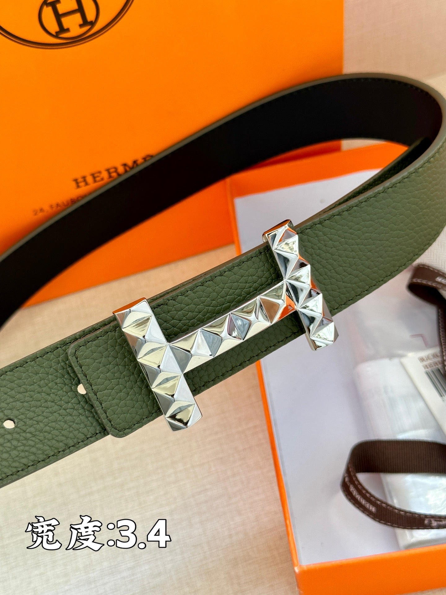 Hermes belt close-up: dark green strap with silver-tone metal H buckle center