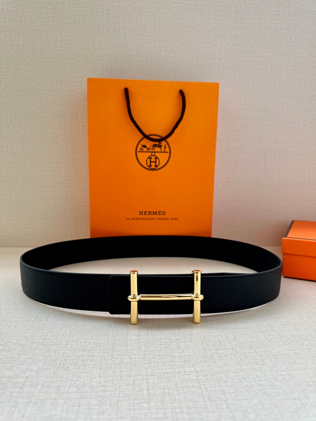 Black leather belt with gold rectangular buckle, laid flat on surface