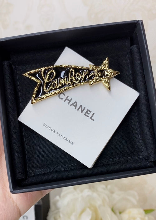 Chanel logo brooch with gold star motif on white card, inside black gift box