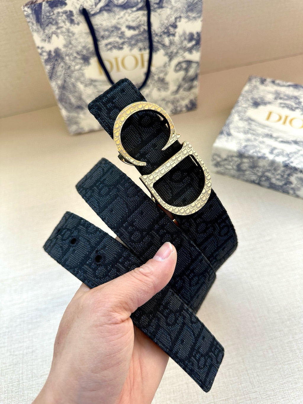 Dior belt close-up held in hand: dark blue strap with gold CD buckle