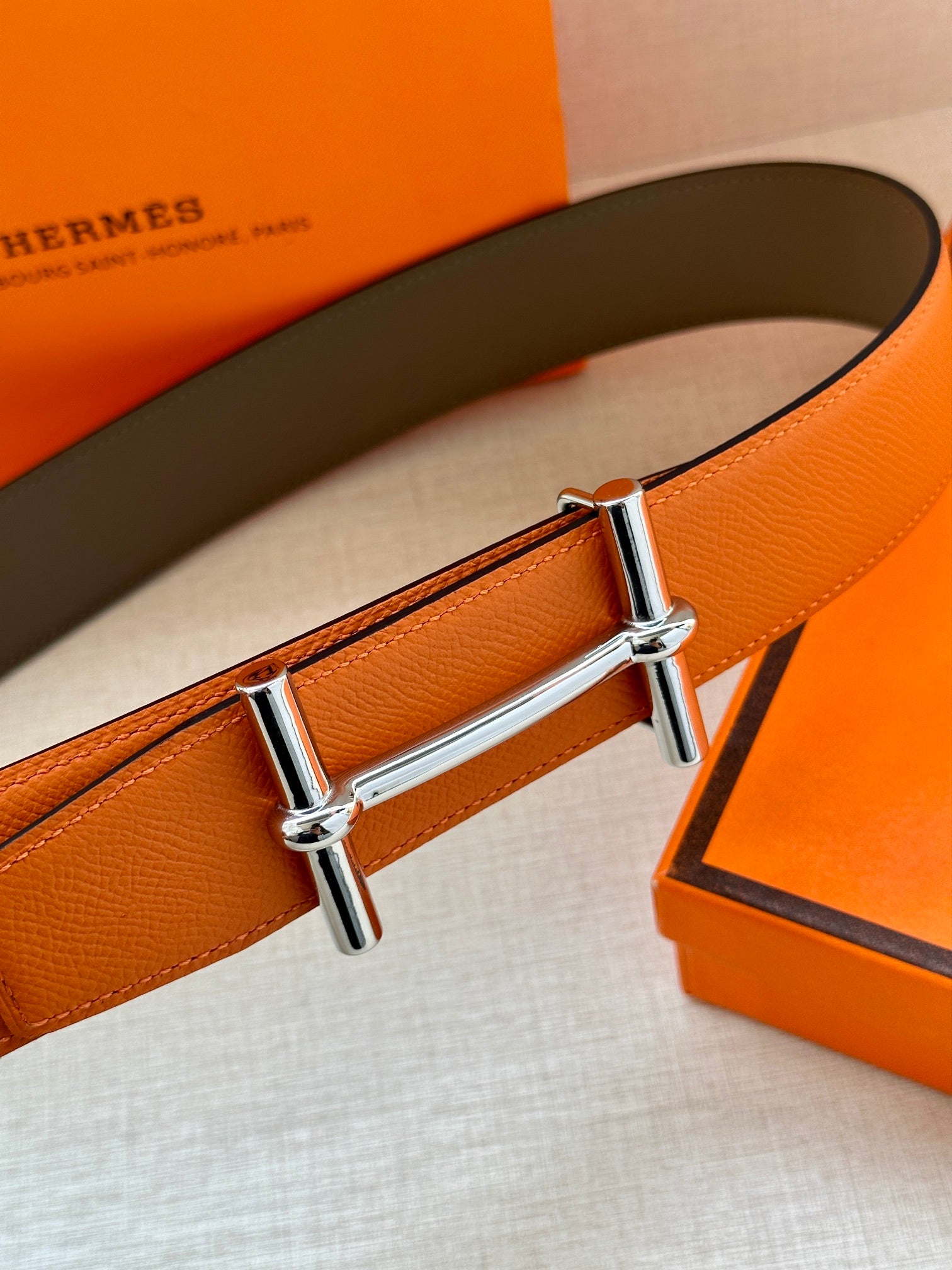 Hermes belt close-up: orange leather with silver rectangular bar buckle
