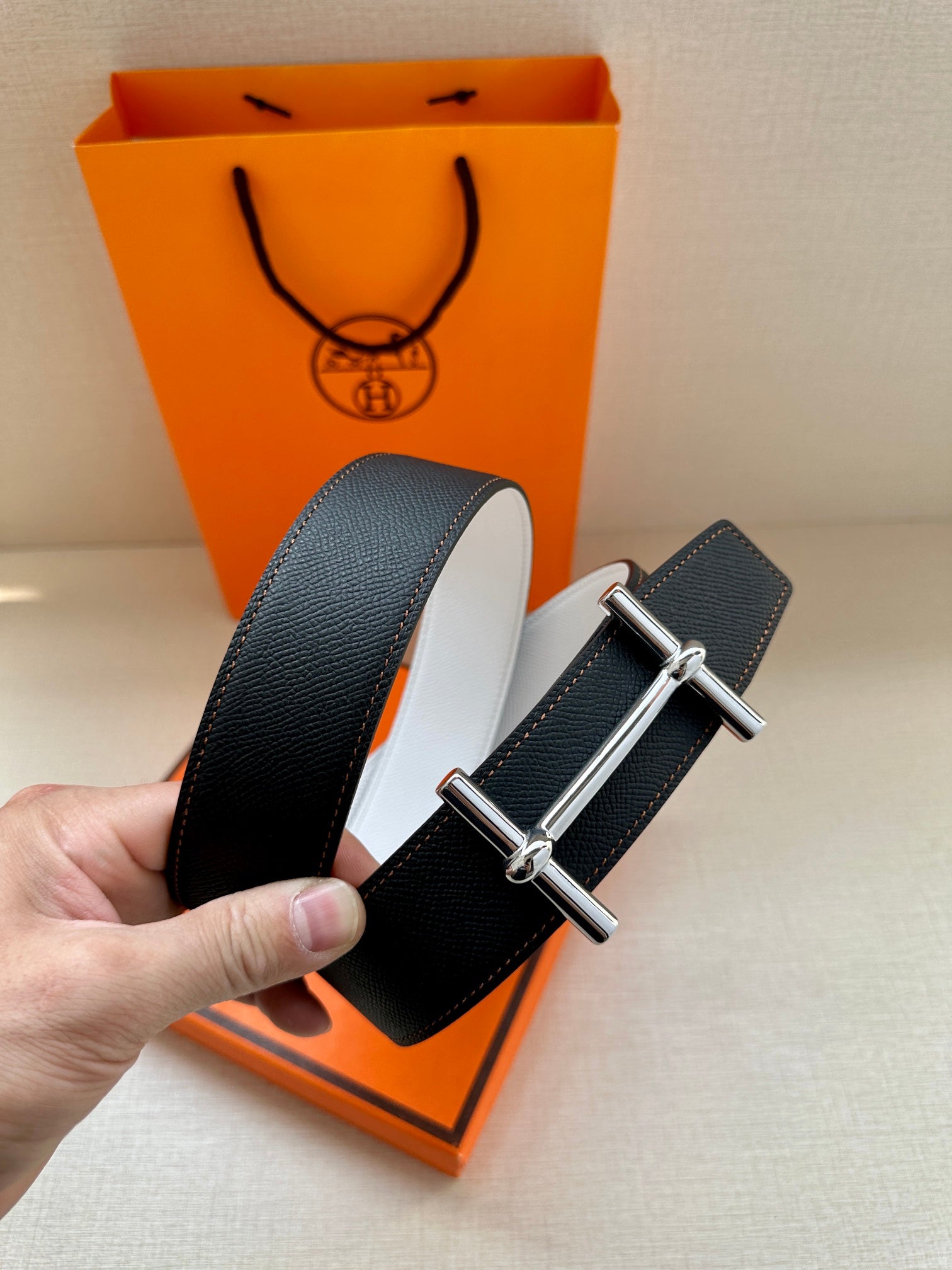 Dark leather belt with silver-tone buckle, strap looped near orange shopping bag.