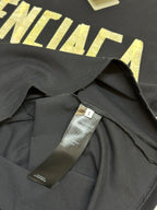 Dark blue T-shirt collar and interior label, with yellow BALENCIAGA letters visible behind.