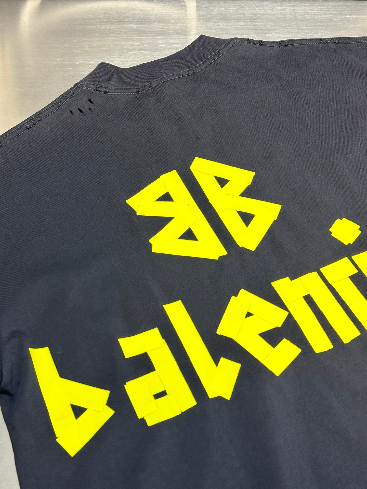 Dark blue Balenciaga T-shirt with large yellow back graphic of stylized letters.