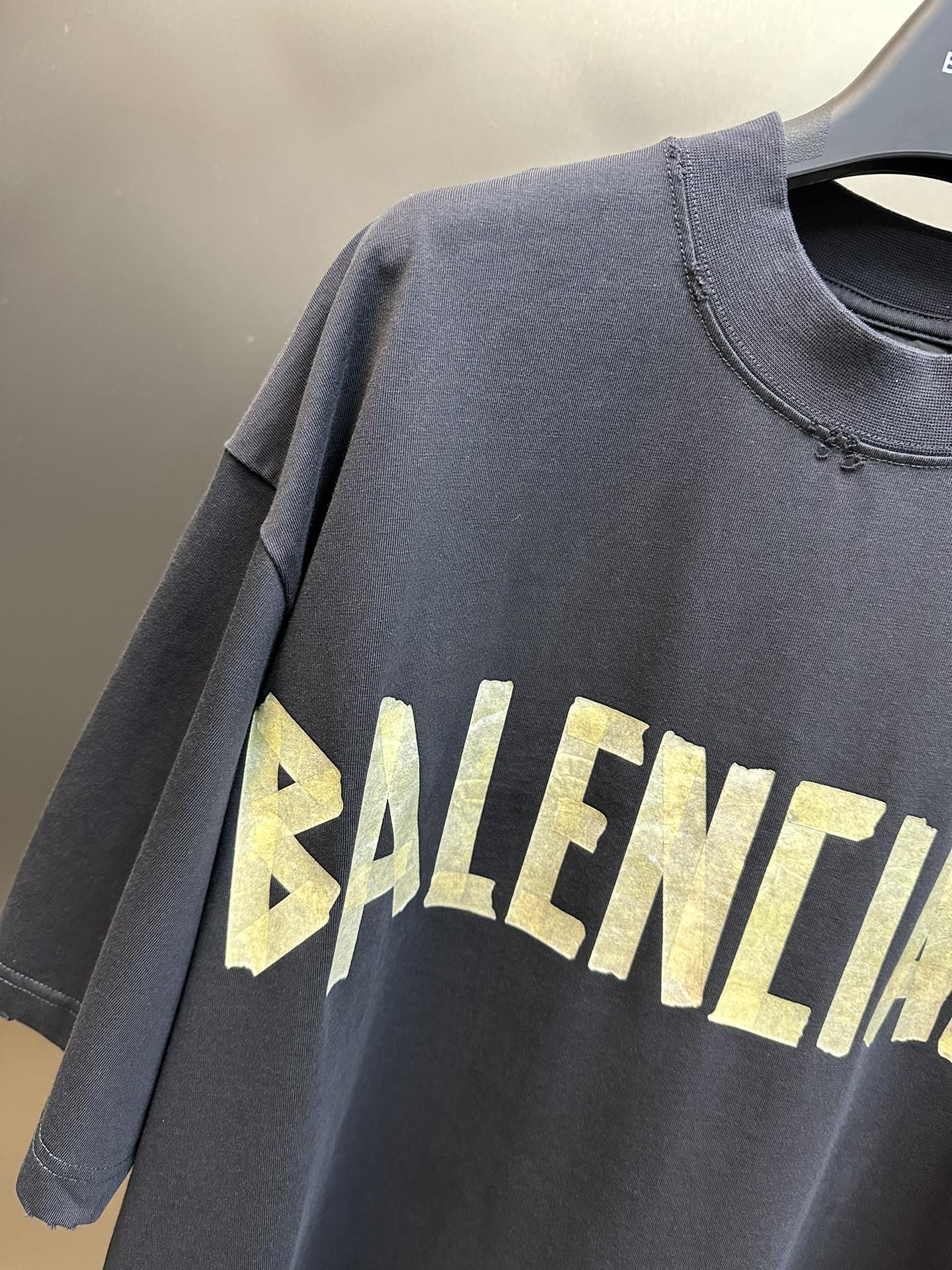 Dark blue T-shirt with textured yellow BALENCIAGA lettering graphic across chest.